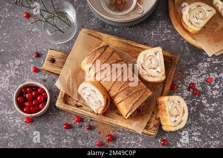 Cutting board with delicious sponge cake roll and fresh cranberries on grey table Stock Photo