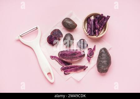 Raw purple potatoes and peeler on pink background Stock Photo