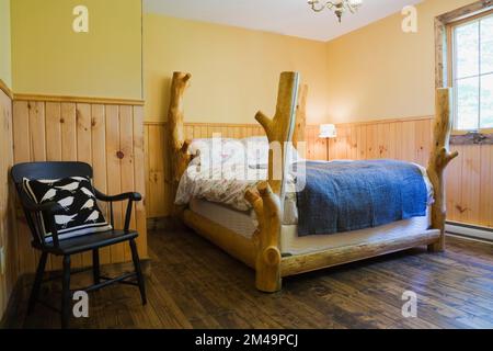 Rustic four poster bed in upstairs guest bedroom with nuanced brown stained floorboards inside log home. Stock Photo