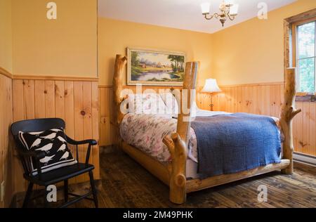 Rustic four poster bed in upstairs guest bedroom with nuanced brown stained floorboards inside log home. Stock Photo