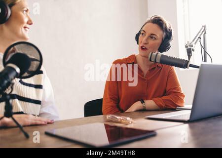 Female radio hosts having a conversation on an audio broadcast. Two women recording an internet podcast in a home studio. Social media influencers cre Stock Photo