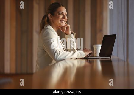 Successful business woman in her 30s is working in a cafe. She has a laptop in front of her, and a confident smile on her face. She appears to be usin Stock Photo