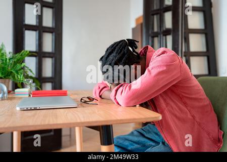 Tired African guy freelancer sleeping at workplace, feeling unmotivated while working from home, Stock Photo