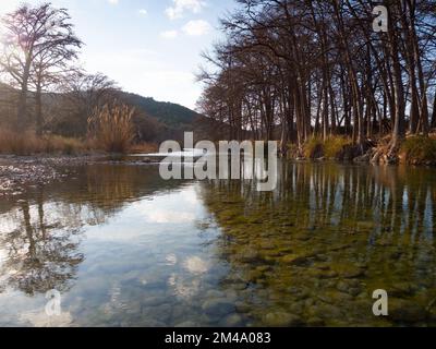 Low angle view over the clear Frio River with stones on riverbed and bald cypress trees lining its riverbank. Photographed in Garner State Park, Texas Stock Photo