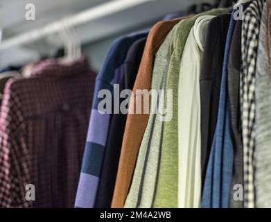 Mens wardrobe clothing hanging on rail in closet. Closeup photo of Men's shirts and sweaters hanging on a rack. Wardrobe clothing hanging on rail in c Stock Photo