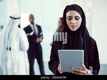 Success is the first thing on her agenda. an attractive young arabic businesswoman working on a tablet in the office with her colleagues in the Stock Photo