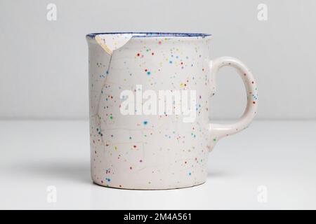 Broken mug on white table. Cracked cup. Stock Photo