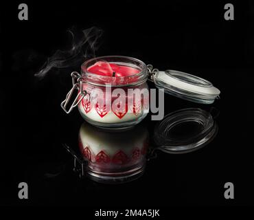 An extinguished candle with smoke on black background with aromas of vanilla, cherry, pomegranate and coconut Stock Photo