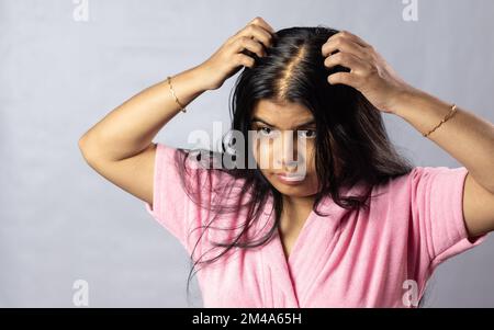 An Indian woman worried due to hair loss problem holds scalp on white background Stock Photo