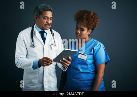 Medical care in the age of the app. Studio shot of two doctors using a digital tablet together against a gray background. Stock Photo