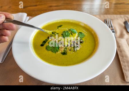 Top view of a broccoli soup in a white bowl. spoon in hand. Stock Photo