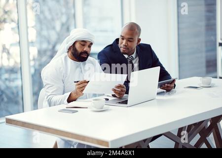 Collaborations work to their companys advantage. two businessmen using a digital tablet and laptop while having a discussion in a modern office. Stock Photo