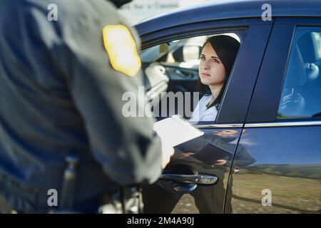 Im gonna have to give you a speeding fine. an unrecognizable male traffic officer issuing a ticket to a female civilian at a roadblock. Stock Photo