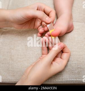 Mother woman sticks a medical adhesive plaster on the toddler baby leg. Mom s hand with sticky wound protection tape and child s foot. Kid aged one ye Stock Photo