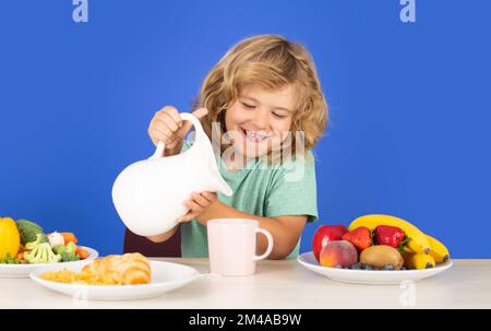 Healthy breakfast lunch for kids. Healthy child pours milk from jug. Funny laughing child pouring milk, studio isolated portrait. Kid with dairy milk. Stock Photo