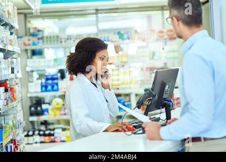I have a customer here...an attractive young female pharmacist helping a male customer in the pharmacy. Stock Photo