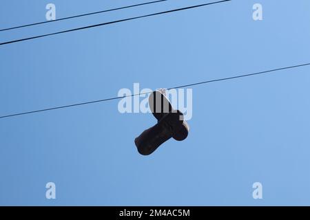 dirty sneakers hang on a wire on a pole against a blue sky Stock Photo