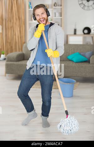 man using a mop as a microphone while doing housework Stock Photo