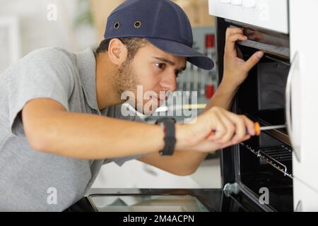 handsome young repairman fixing oven with screwdriver Stock Photo