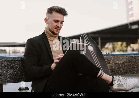 Man using a tablet while sitting next to a skateboard Stock Photo