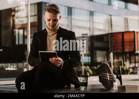 Stylish man using a tablet sitting next to a skateboard Stock Photo