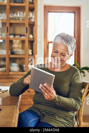 Shes no stranger to the digital world. a mature woman using a digital tablet at home. Stock Photo