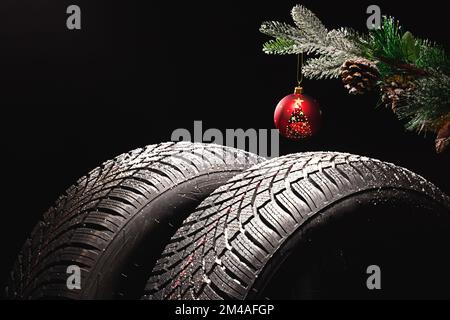 Winter Car tire for snow and Christmas tree ball and decoration isolated on black background. New automobile tyre for snowy road. Stock Photo