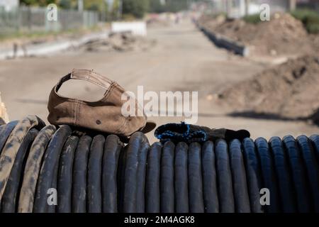 baseball cap and construction gloves lie on a black cable left by the builder in the sun Stock Photo