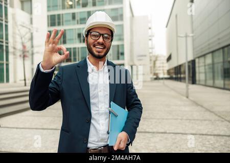 Indian construction architect in suit and hardhat with paper folder in hands against modern building Stock Photo