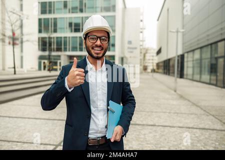 Indian construction architect in suit and hardhat with paper folder in hands against modern building Stock Photo