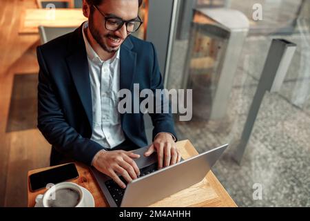 Smiling Indian businessman working on laptop in coffee shop working space Stock Photo
