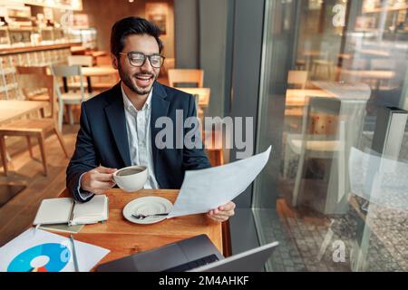 Smiling indian businessman drinking coffee and working with documents in cafe Stock Photo