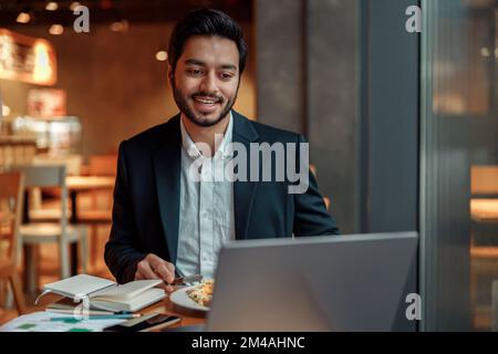 Handsome indian businessman working on laptop in cozy cafe sitting near window Stock Photo