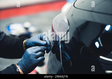 Close up of person wearing blue gloves working on tail light of black car in a garage. Car detailing. Horizontal indoor shot . High quality photo Stock Photo
