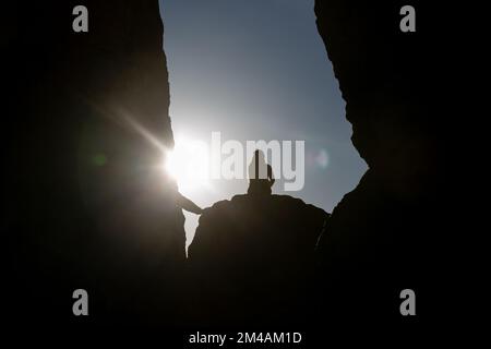 silhouette of a young couple sitting on a rock looking at the sunset. Stock Photo