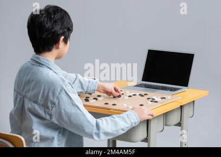 Cute Chinese boy playing the game of Go with laptop Stock Photo