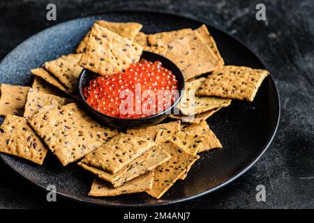 Red fresh trout fish caviar in a bowl served with sesame seed crackers on concrete table background Stock Photo