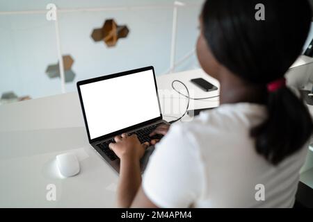 Back view anonymous African American woman using laptop with blank screen and graphic tablet to create illustration during work on creative project in Stock Photo