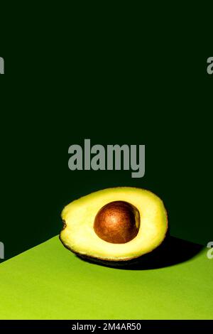 Half of ripe avocado with seed placed on corner of table against dark green background Stock Photo