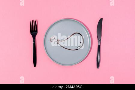Top view of black plastic fork and knife placed on pink table on gray plate with painted cartoon chicken drumstick Stock Photo