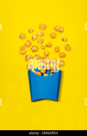 Top view of bright blue paper bag with delicious scattered sweet caramel popcorn on yellow background Stock Photo