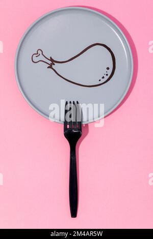 Top view of black plastic fork placed on pink table on gray plate with painted cartoon chicken drumstick Stock Photo