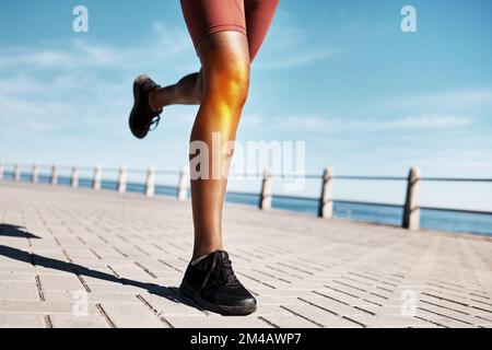 Black woman runner, knee pain and legs by promenade, street or training by ocean in fitness, speed or health. Feet, sneakers and running on road by Stock Photo