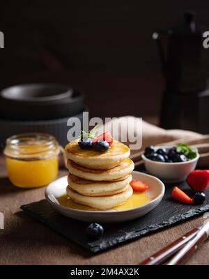 Delicious homemade pancakes with strawberries and blueberries and honey on a dark wooden background with coffee pot. The concept of a healthy and nutr Stock Photo