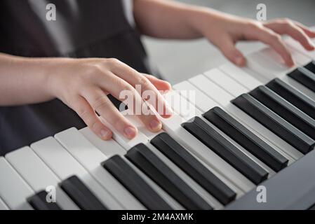 Hobby concept. A  girl in a gray dress plays an electronic piano. Morning lifht on window. Close up image Stock Photo