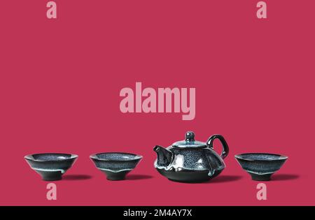 Dark blue clay teapot and small cups lined on trendy magenta color of year 2023 background. Creative minimalist tea ceremony concept. Copy space. Stock Photo