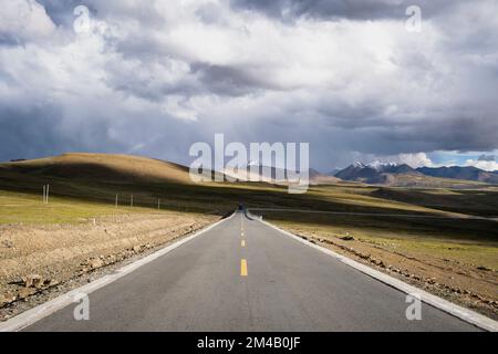 Road crosses the Tibetan plateau with snow-capped mountains in the background. Tibet Autonomous Region. China. Stock Photo
