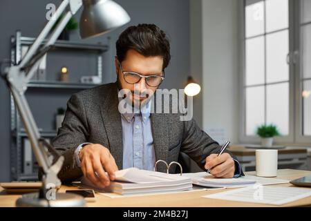 Male bookkeeper sitting at an office desk, doing paperwork, and reading documents Stock Photo