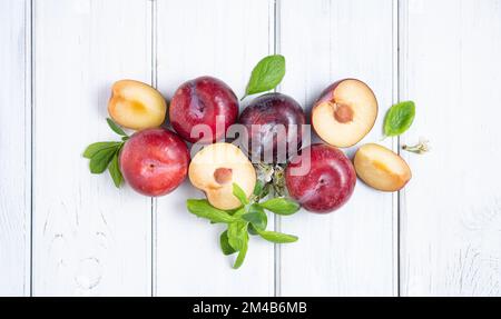 Concept flatlay with juicy red plums and green leaves on a white wood background. Top view image Stock Photo