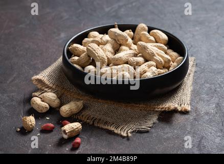 unpeeled peanuts in a black bowl on a dark texture  background. Macro and close up image. Stock Photo